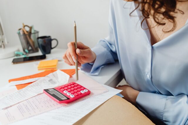 Proprietara unui magazin mic care face calcule cu un calculator și un carnet, la tejgheaua magazinului