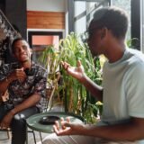 Două prietene care discută la o cafea, una dintre ele recomandând celeilalte un serviciu folosit recent