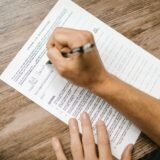 Persoană care completează un formular fiscal pe laptop, cu documente și extrase de cont alături
